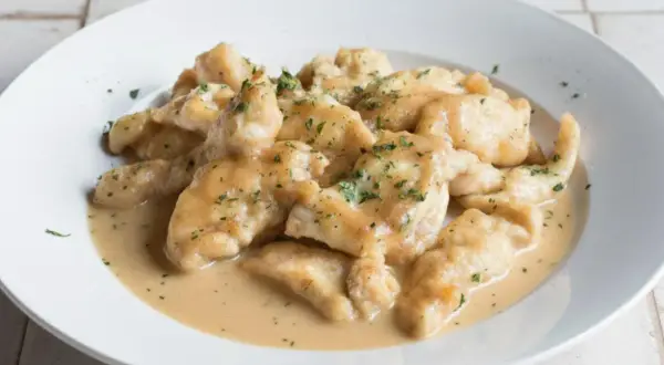 Straccetti di pollo cremosi, teneri bocconcini di pollo in una salsa vellutata, guarniti con prezzemolo tritato.