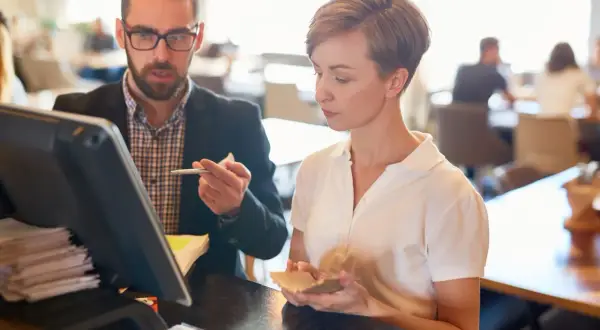 Mann mit Brille und Frau besprechen etwas am Kassensystem in einem Restaurant.