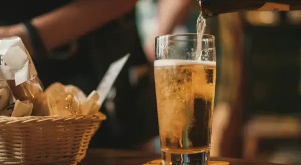 Z butelki leje się złociste piwo IPA do szklanki. Obok koszyk z pieczywem.