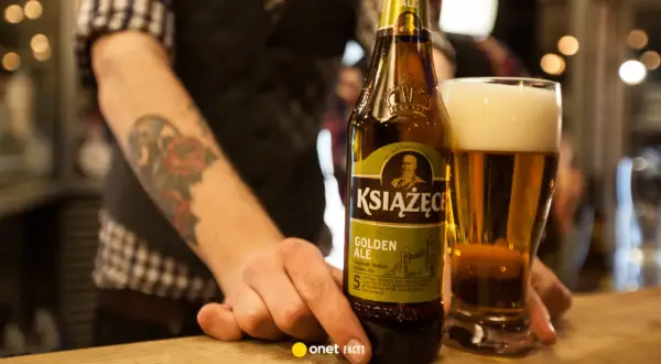 Ręka z tatuażem sięga po butelkę piwa Książęce Golden Ale. Czy to piwo jest gorzkie?