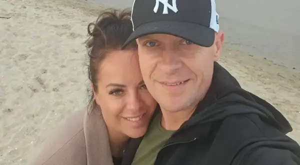 Piotr Marciniak z żoną na plaży, uśmiechnięci i blisko siebie.