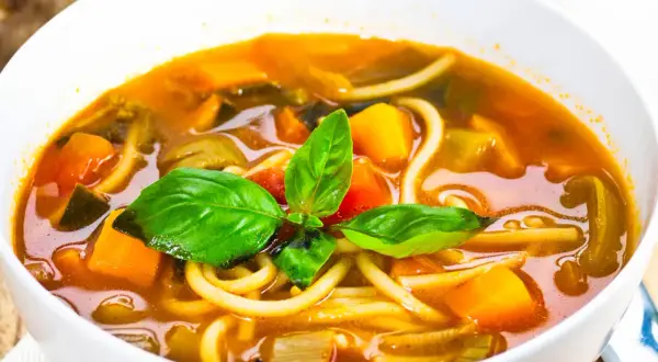 Una ciotola di pasta con i tenerumi, ricca di verdure colorate e basilico fresco. Un piatto confortante e salutare.