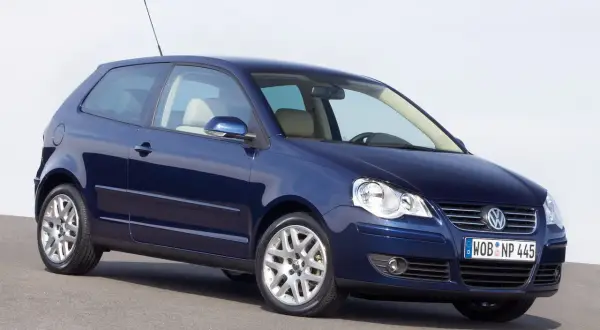 Granatowy Volkswagen Polo 2003, trzydrzwiowy, z jasnym wnętrzem, stoi na szarej nawierzchni.