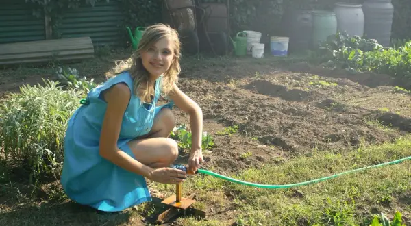 Dziewczyna w niebieskiej sukience podlewa grządki. Idealna ziemia pod uprawę jagody kamczackiej.