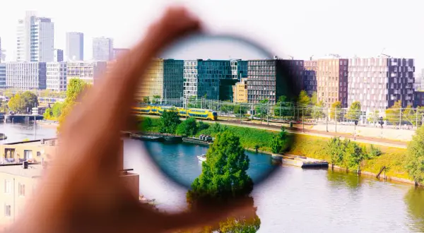 Dłoń trzyma okrągły filtr, przez który widać miasto z pociągiem. Efekt filtrów w fotografii.