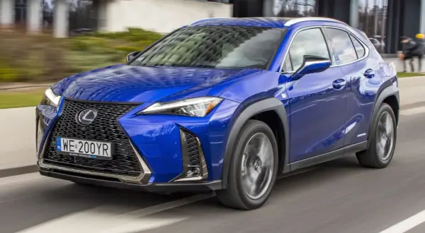 Błękitny Lexus UX 200 w ruchu miejskim, z widocznym grillem i reflektorami.