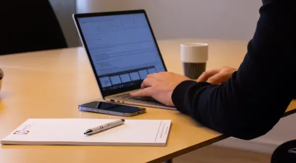 Person arbetar vid laptop, med mobil och anteckningsblock på bordet. Kanske planerar att låna ut pengar till aktiebolag.
