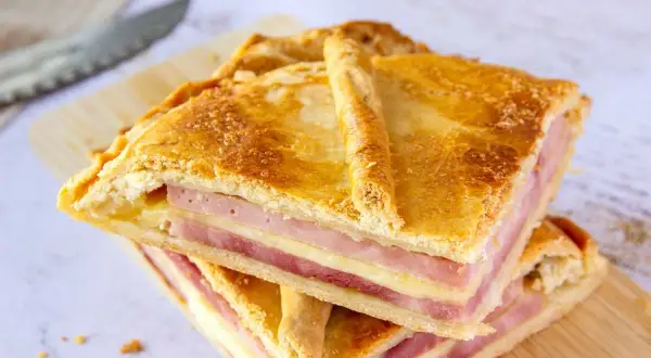 Dos porciones de empanada de jamón y queso apiladas, con masa dorada y relleno visible.