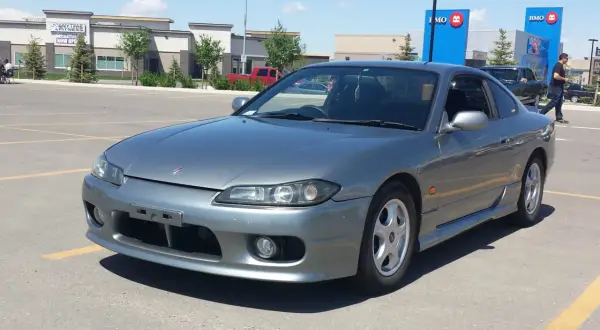 Szary Nissan Silvia s15 na parkingu przed budynkami BMO i Anytime Fitness.