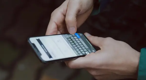 Dłonie trzymają smartfon, na ekranie widać klawiaturę i tekst. To jak instrukcja obsługi telefonu, którą ktoś właśnie czyta.