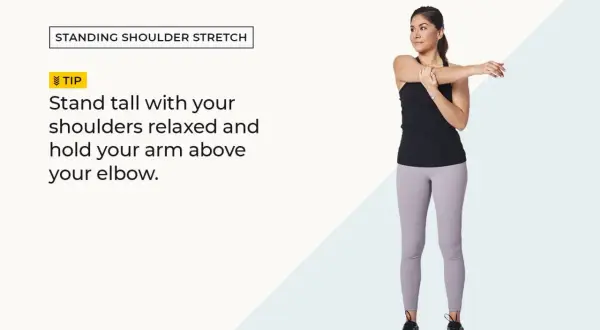 Woman performing standing shoulder stretches, holding one arm across her chest.