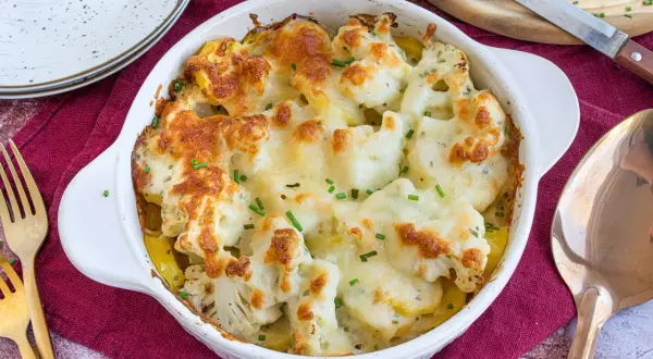 Ein goldbraun überbackener Blumenkohl Kartoffel Auflauf mit geschmolzenem Käse und frischen Kräutern, bereit zum Servieren.