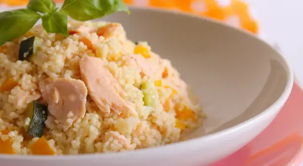 Un gustoso cous cous con salmone, zucchine e peperoni, condito con un tocco di salsa di soia e guarnito con basilico fresco.