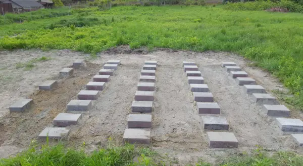 Przygotowana wylewka pod domek narzędziowy. Ułożone bloczki betonowe tworzą fundament na piaszczystym podłożu.