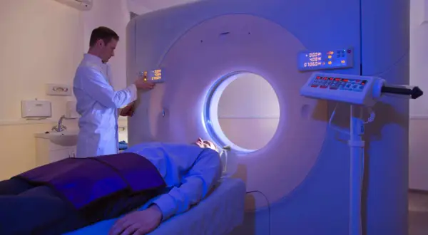Arzt bedient CT-Scanner, Patient liegt auf Liege. Die CT-Strahlenbelastung wird minimiert.