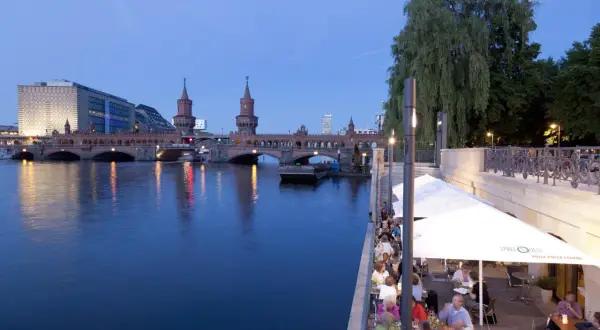 Abendstimmung an den Rivo SpreeTerrassen: Gäste genießen das Ambiente am Wasser mit Blick auf die Oberbaumbrücke.