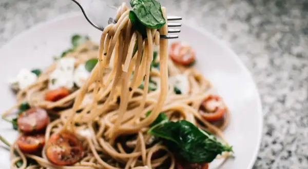 Widok z bliska na makaron z pesto ze słoika i śmietaną, z pomidorkami koktajlowymi i mozzarellą.