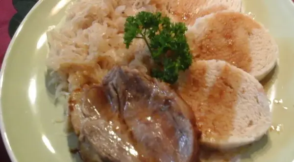 Ein Teller mit tschechischem Schweinebraten, Sauerkraut und Knödeln, garniert mit Petersilie.