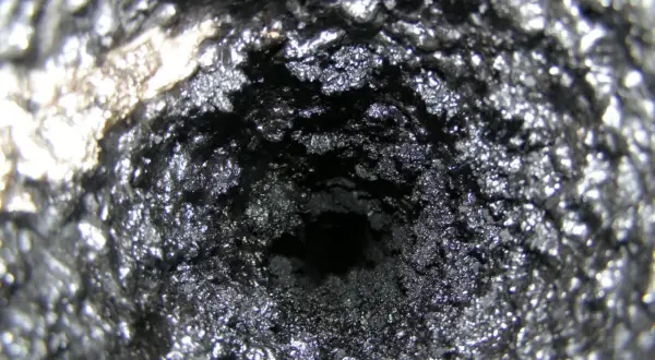 Wnętrze komina pokryte grubą warstwą sadzy i kreozotu, tworzącą chropowatą, ciemną powierzchnię.