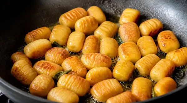 Gnocchis dorés et légèrement grillés dans une poêle, prêts pour la cuisson finale.