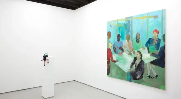 A miniature figure climbs a pedestal in a white-walled gallery, a vibrant painting of a diverse group at a meeting hangs nearby. NYC galleries for emerging artists showcase such intriguing pieces.
