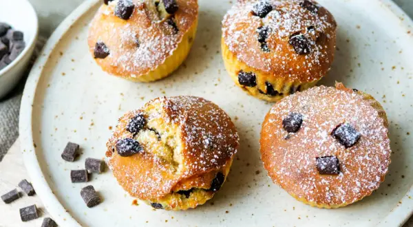 Vier leckere Schoko-Muffins, frisch aus dem Airfryer, mit Puderzucker bestäubt und Schokostückchen.