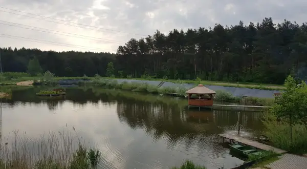 Malownicze łowisko Trzy Stawy z altaną na wodzie, małą wyspą i zieloną łódką przy pomoście.