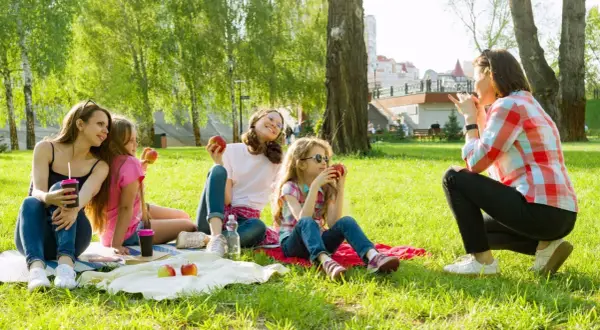 Rodzina na pikniku w parku. Czy Boże Ciało jest dniem wolnym od pracy? Dzieci jedzą jabłka, ciesząc się słońcem.