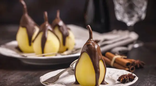 Poires pochées nappées de chocolat, un délice de poire belle Hélène. Cannelle et anis étoilé en arrière-plan.