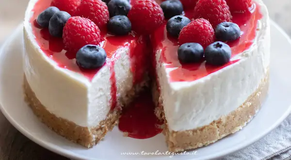 Cheesecake ricetta: torta cremosa con base croccante, guarnita con lamponi, mirtilli e coulis rosso.