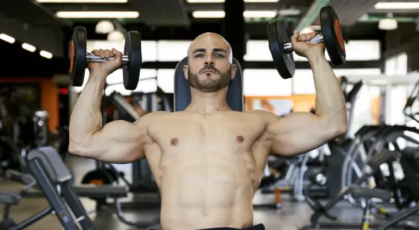 Uomo calvo con barba solleva manubri in palestra, allenamento per il **total body**.
