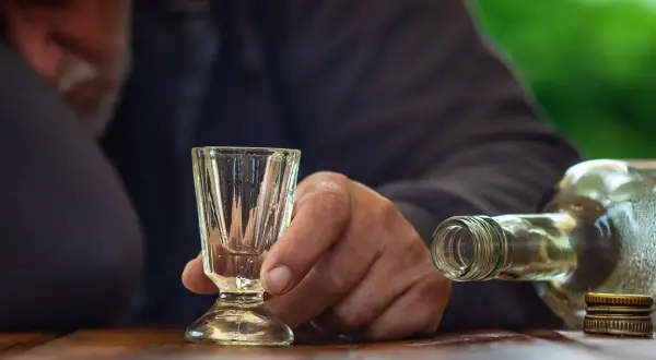 Dłoń trzyma puste kieliszek obok butelki alkoholu.