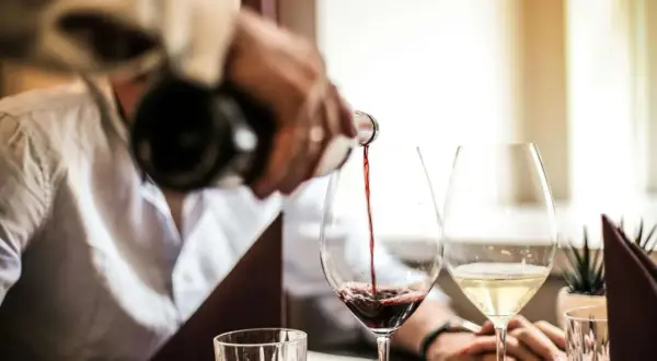 Versando vino rosso in un calice, scoprendo il significato di vino fermo. Accanto, un bicchiere di vino bianco.