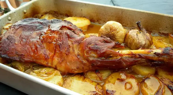 Paletilla de cordero al horno, dorada y jugosa, con patatas y ajos asados. El tiempo y temperatura perfectos para un plato delicioso.