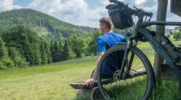 Mężczyzna odpoczywa na ławce po przejażdżce rowerem po Beskidach. Piękny widok na góry i lasy.