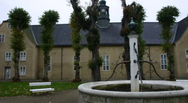 Fontanna przed żółtym budynkiem z wieżą kościelną. Spacerując po **most Niemcy Dania**, można podziwiać architekturę.