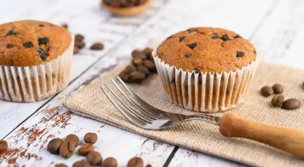 Dwa muffinki z kawałkami czekolady, ziarna kawy i widelec. Idealne na śniadanie, gdy zastanawiasz się, jak długo piec muffinki.