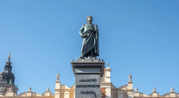 Pomnik Adama Mickiewicza, symbol romantyczności, na tle błękitnego nieba i zabytkowych kamienic.