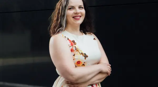 Uśmiechnięta kobieta w kwiecistej sukience, szukająca tanich sukienek plus size na wesele.