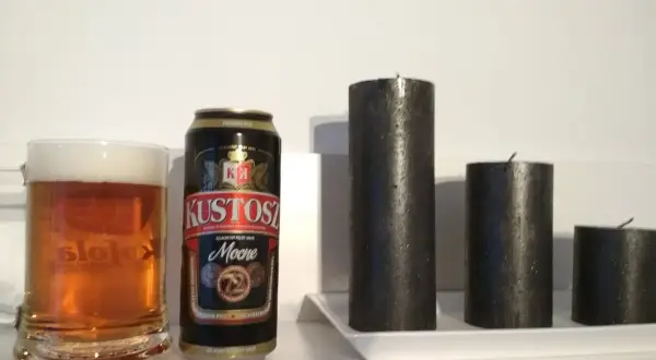 Kufel piwa i puszka Kustosz Mocne obok trzech czarnych świec.