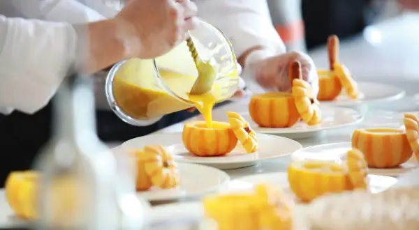 Szef kuchni, pomoc kuchenna kod zawodu, nalewa zupę dyniową do wydrążonych dyń.