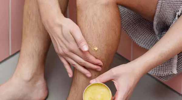 Hände tragen eine gelbe Salbe auf ein Bein auf. Manche glauben, sheabutter trocknet haut aus, aber diese Salbe spendet Feuchtigkeit.