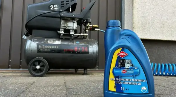 Niebieska butelka z napisem "OLEJ DO SPRĘŻAREK TŁOKOWYCH PISTON COMPRESSOR OIL" obok sprężarki.