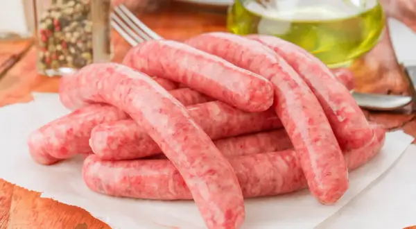 Świeża kiełbasa na papierze, obok przyprawy i oliwy. Zastanawiasz się, ile może leżeć kiełbasa w lodówce?