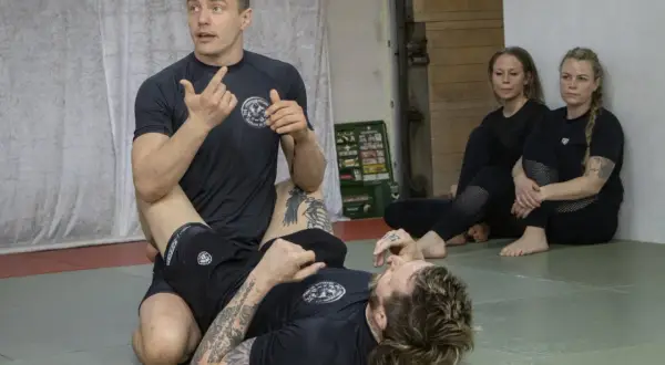 Instruktör visar en teknik i stark bjj. Två kvinnor sitter och observerar.