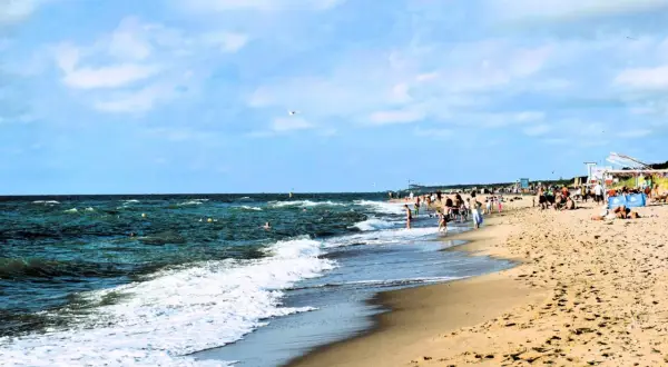 Plaża w Dąbkach tętni życiem. Ludzie kąpią się w morzu, spacerują brzegiem, a na piasku odpoczywają. To idealne miejsce na wakacyjne atrakcje.