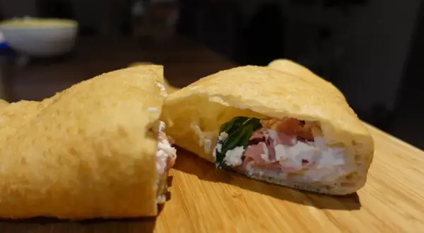 Une pizza frite napolitaine, garnie de ricotta, jambon et basilic, sur une planche en bois.