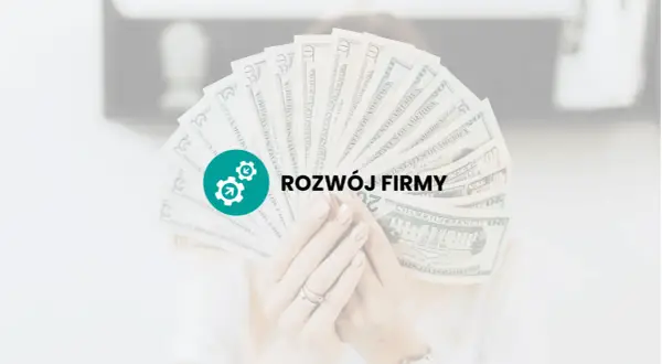 Dłoń trzyma wachlarz banknotów dolarowych z ikoną i napisem "ROZWÓJ FIRMY".