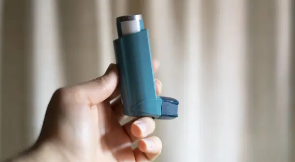Dłoń trzyma niebieski inhalator z salbutamolem, gotowy do ulgi w ataku astmy.