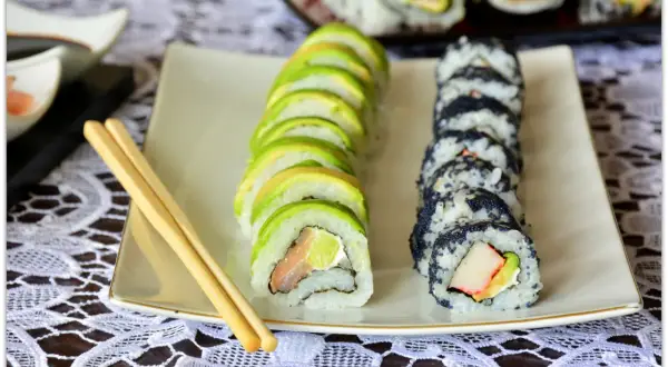 Jak pokroić awokado do sushi? Na talerzu sushi z awokado i czarnym kawiorem, obok pałeczki.